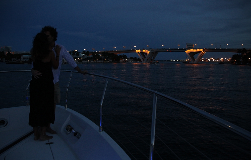 Couple embraces at dinner cruise under illuminated bridge, Fort Lauderdale evening